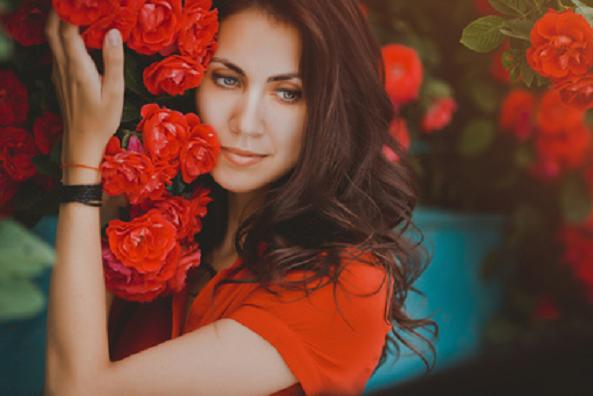 Beautiful portrait of sensual brunette woman close to red roses. Toned image