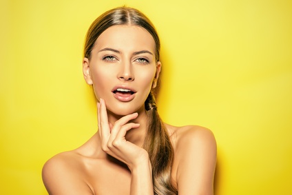 Smiling young woman with natural make-up posing over bright yellow background. Copy space. Cosmetics. Skincare, bodycare.